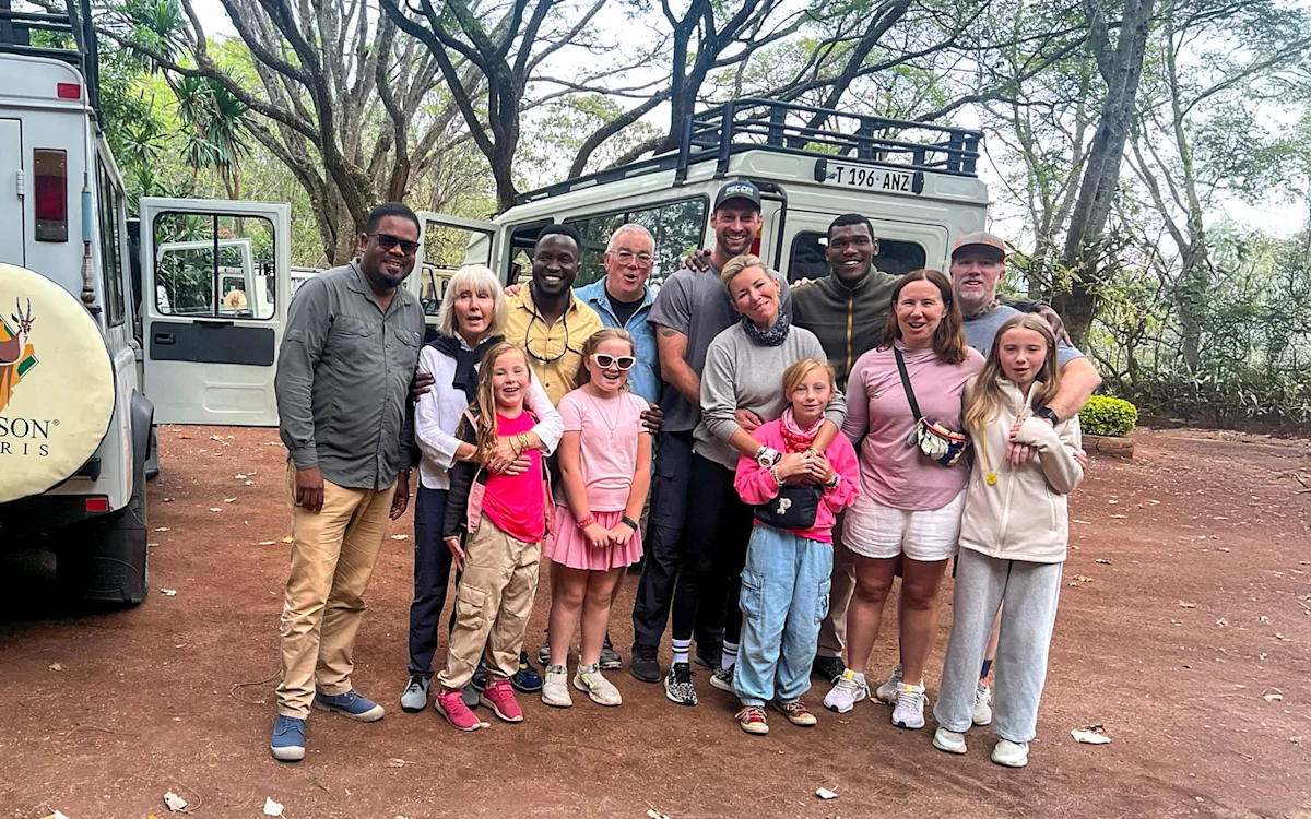 Multigenerational family with Thomson Safaris guides beside safari vehicles