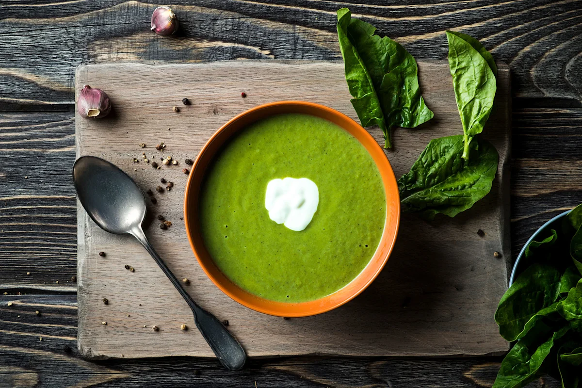 Bowl of creamy spinach soup with a swirl of cream beside fresh spinach leaves