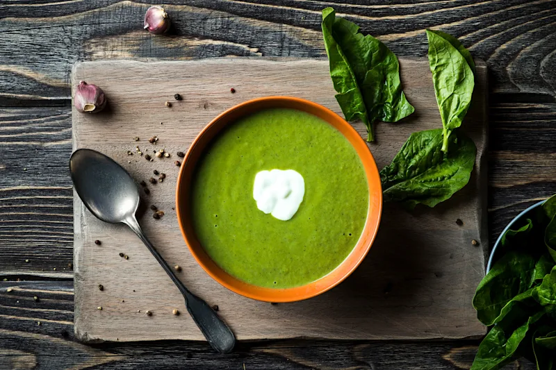 Bowl of creamy spinach soup with a swirl of cream beside fresh spinach leaves