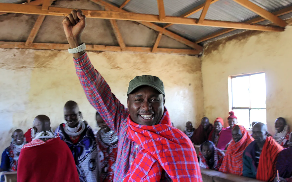 Daniel Yamat raising his fist in a classroom full of Maasai community members