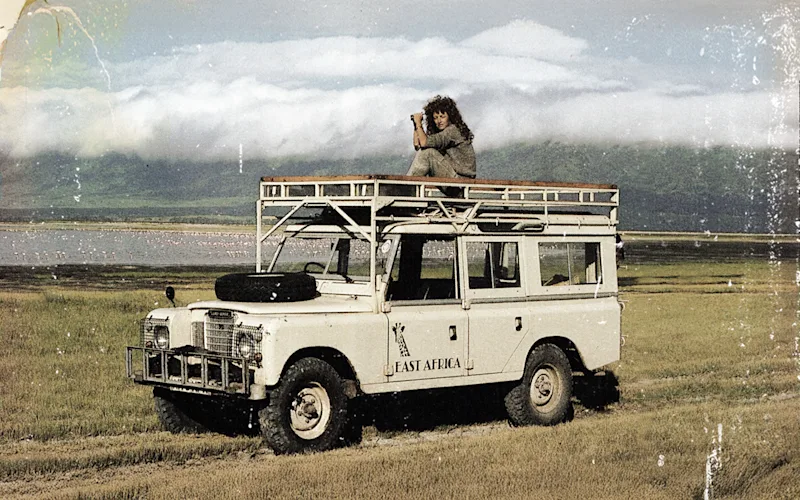Thomson Safaris co-founder Judi Wineland on the roof of a vintage Land Rover in Tanzania in the 1980s