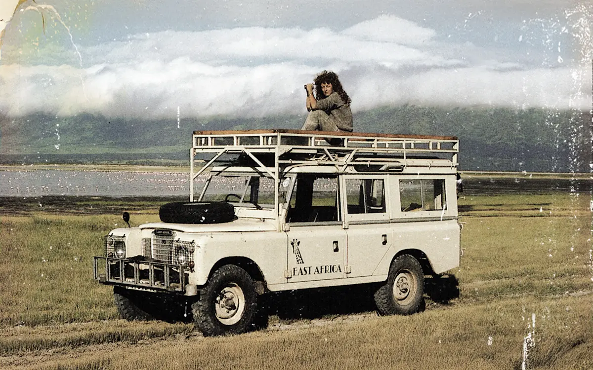Thomson Safaris co-founder Judi Wineland on the roof of a vintage Land Rover in Tanzania in the 1980s