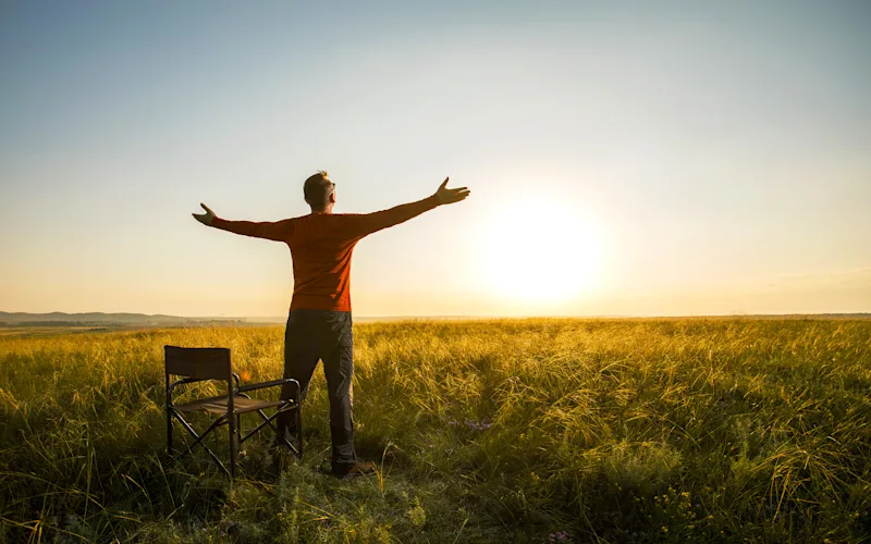 Safari guest with arms outstretched in savanna grass at sunrise