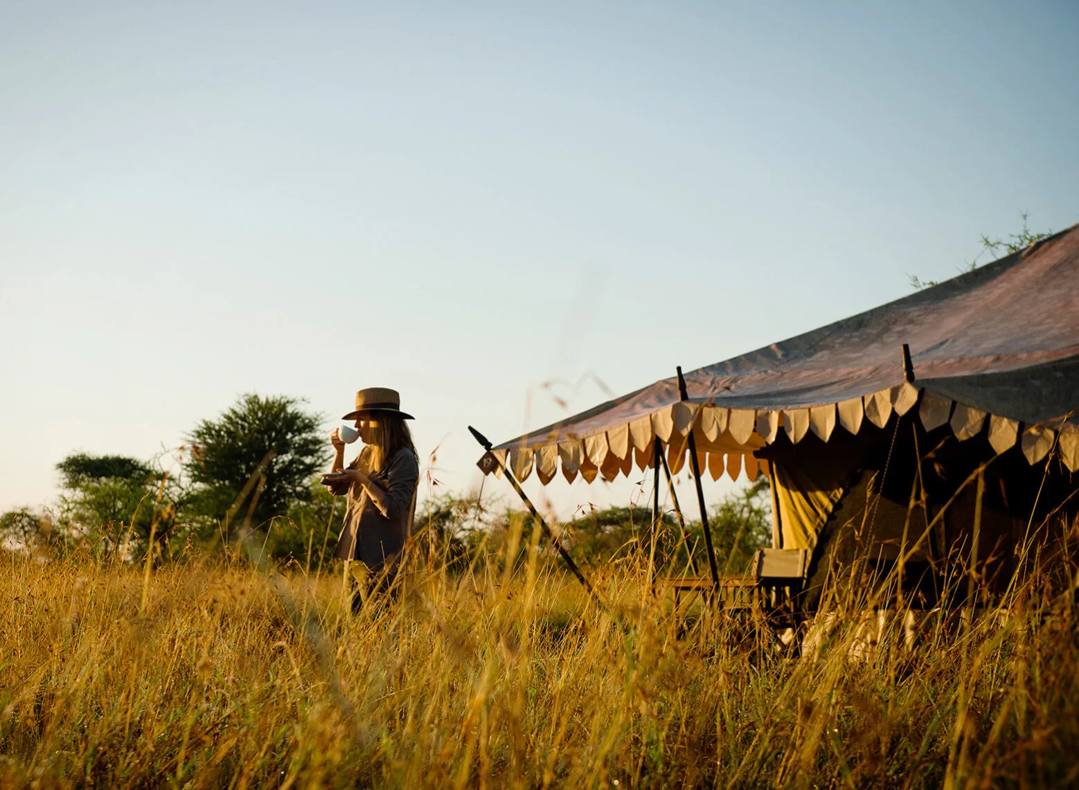 Guest sipping coffee in tall golden grass beside a tent at Serengeti Nyumbas