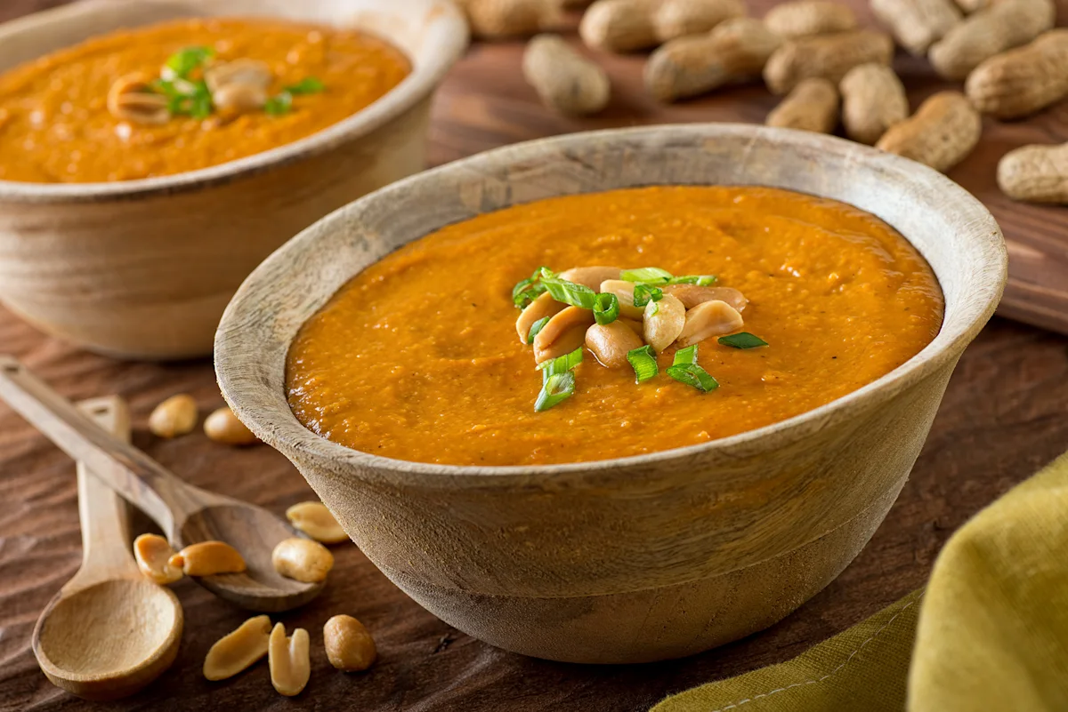 Bowls of pea and peanut butter soup surrounded by peanuts