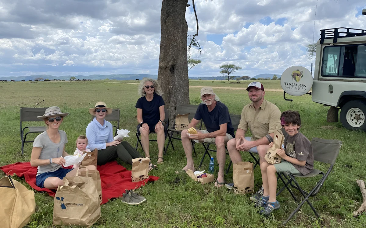 The Thomson founders' family enjoying a picnic under a tree beside a safari vehicle