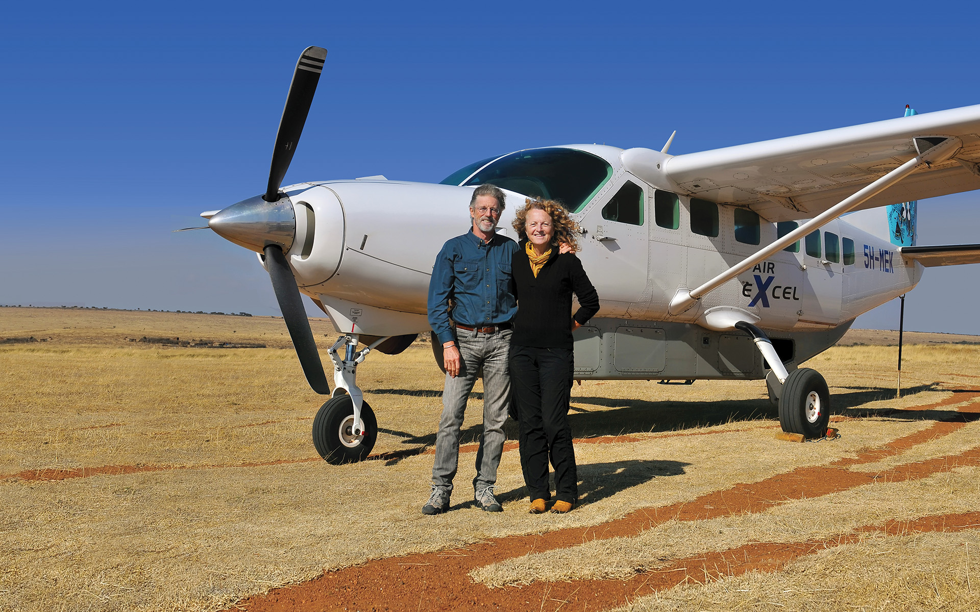 Founders Rick Thomson and Judi Wineland standing beside a small bush plane on a dirt airstrip