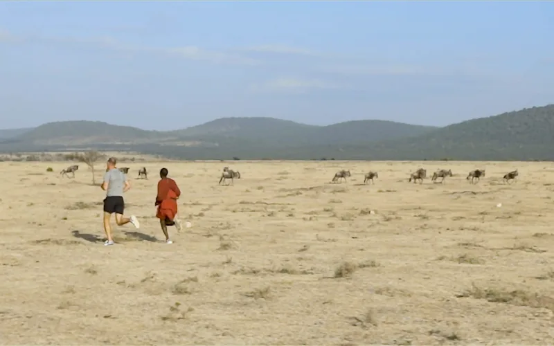 Safari guest jogging with a Maasai runner across the Serengeti plains