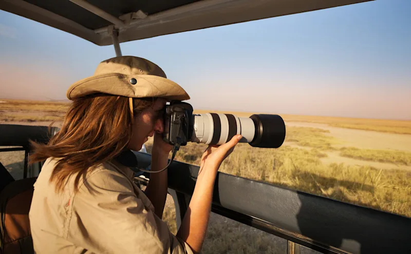 Woman photographing with a long telephoto lens from a safari vehicle