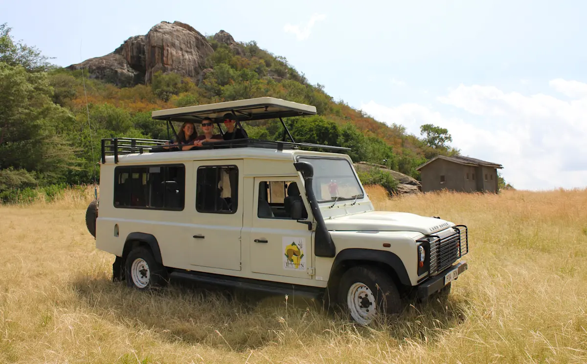 Safari vehicle parked in tall grass below a rocky kopje in the Serengeti