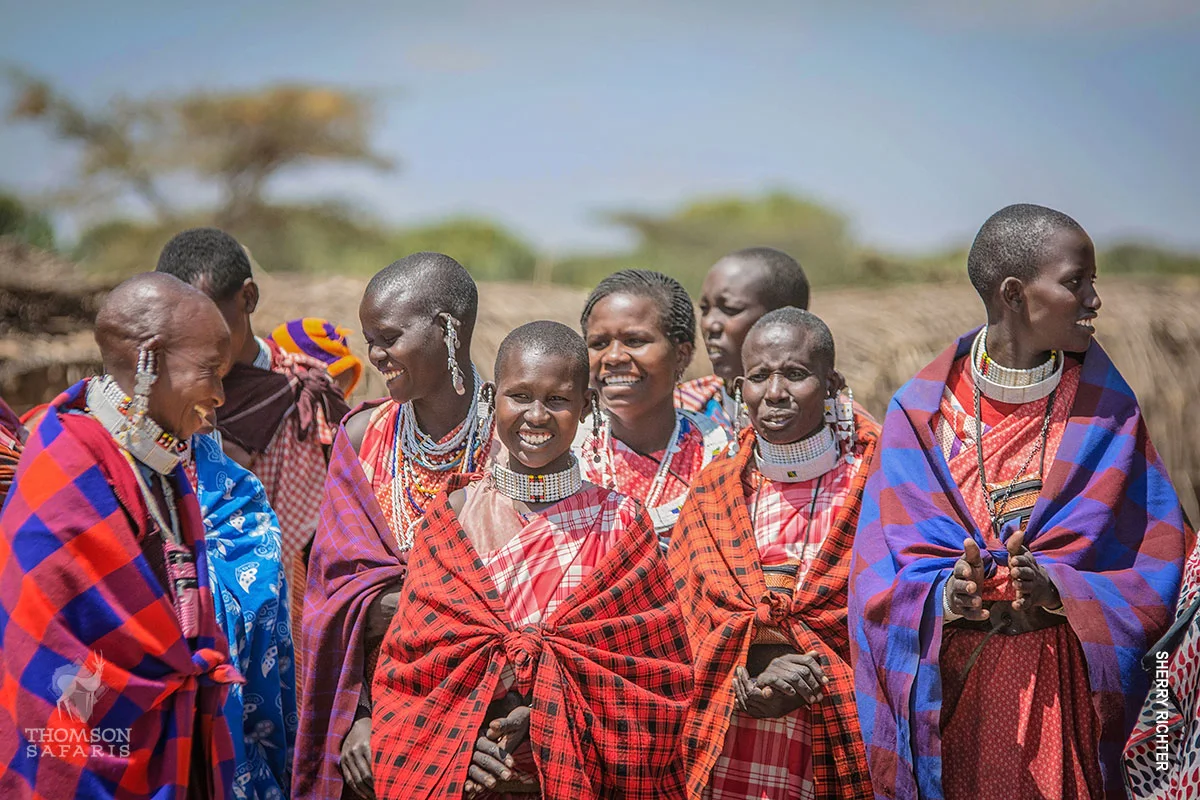 Smiling Maasai women in red shúkà wraps and beaded collars