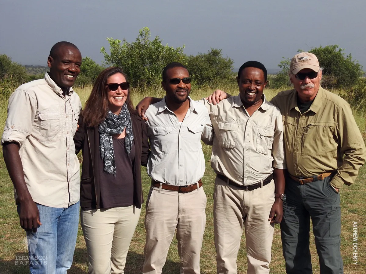 Five people in safari clothes posing arm in arm on the grassy plains