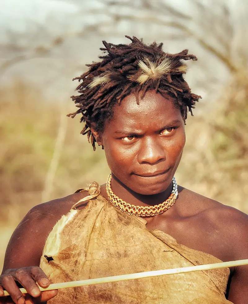 Hadza hunter with a bow, wearing a hide wrap and beaded necklace