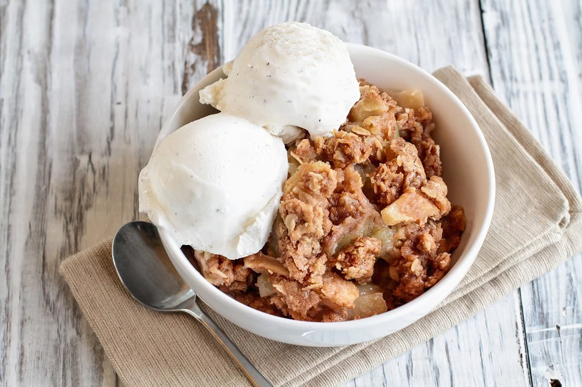 Apple crisp topped with two scoops of vanilla ice cream
