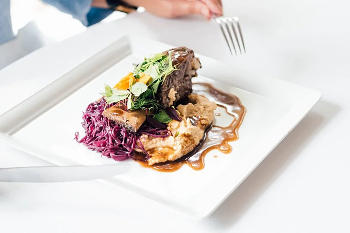 Plated ribs with red cabbage, roasted vegetables and greens