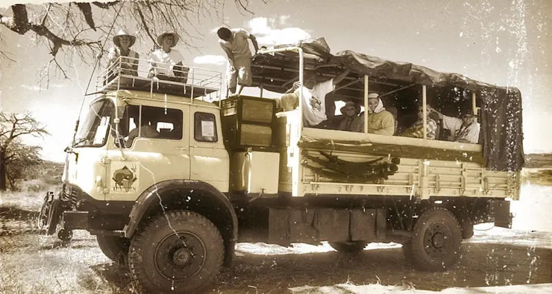 Faded vintage print of guests riding on the roof of an early Bedford safari truck