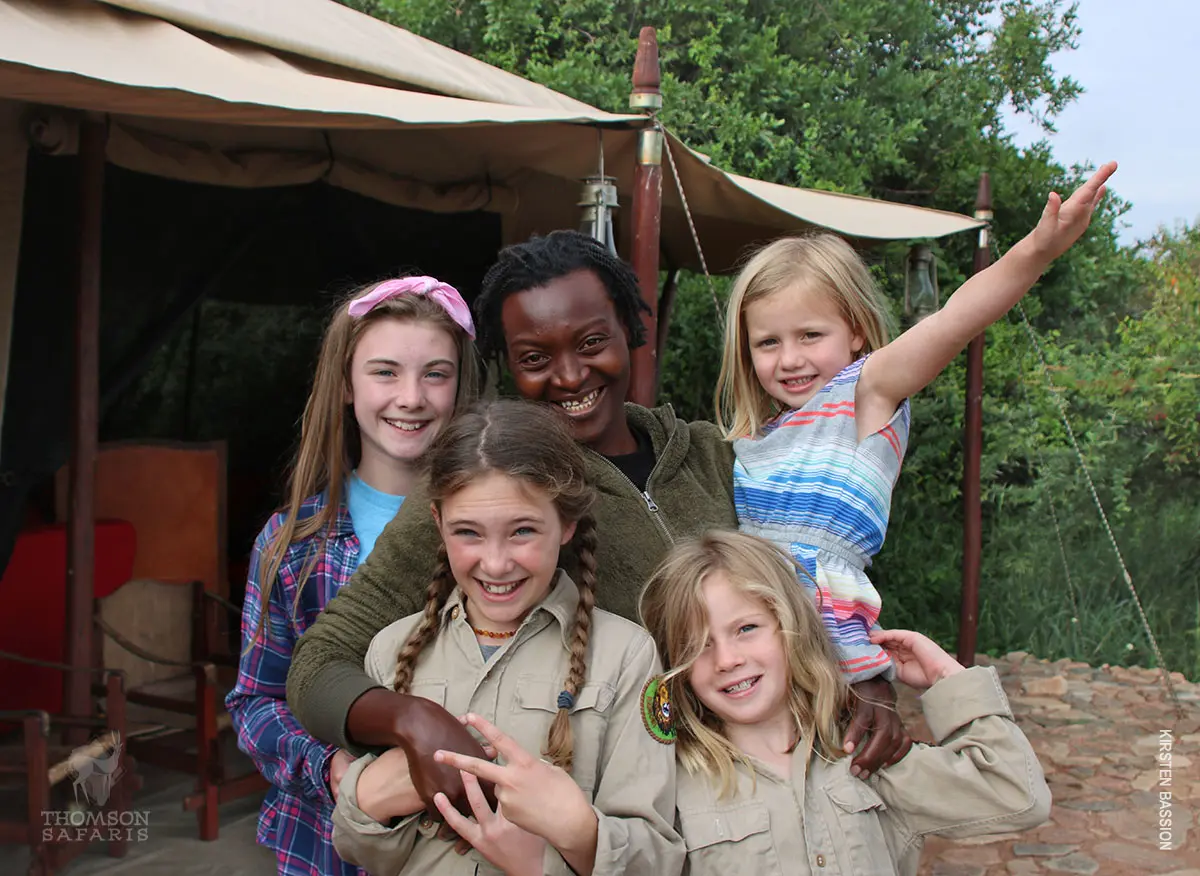 Smiling guide posing with four young girls outside a safari tent