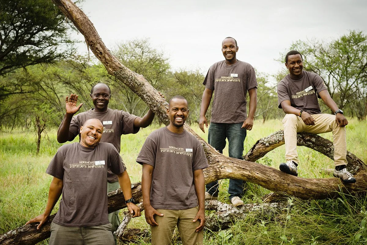 Five camp staff in matching T-shirts posing around a fallen tree