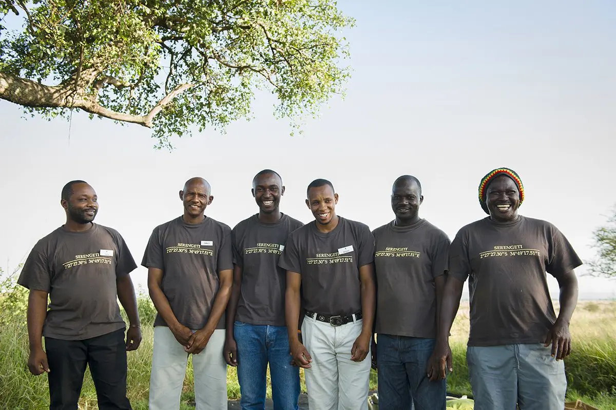 Six Thomson camp staff in matching t-shirts standing together under a tree in the Serengeti