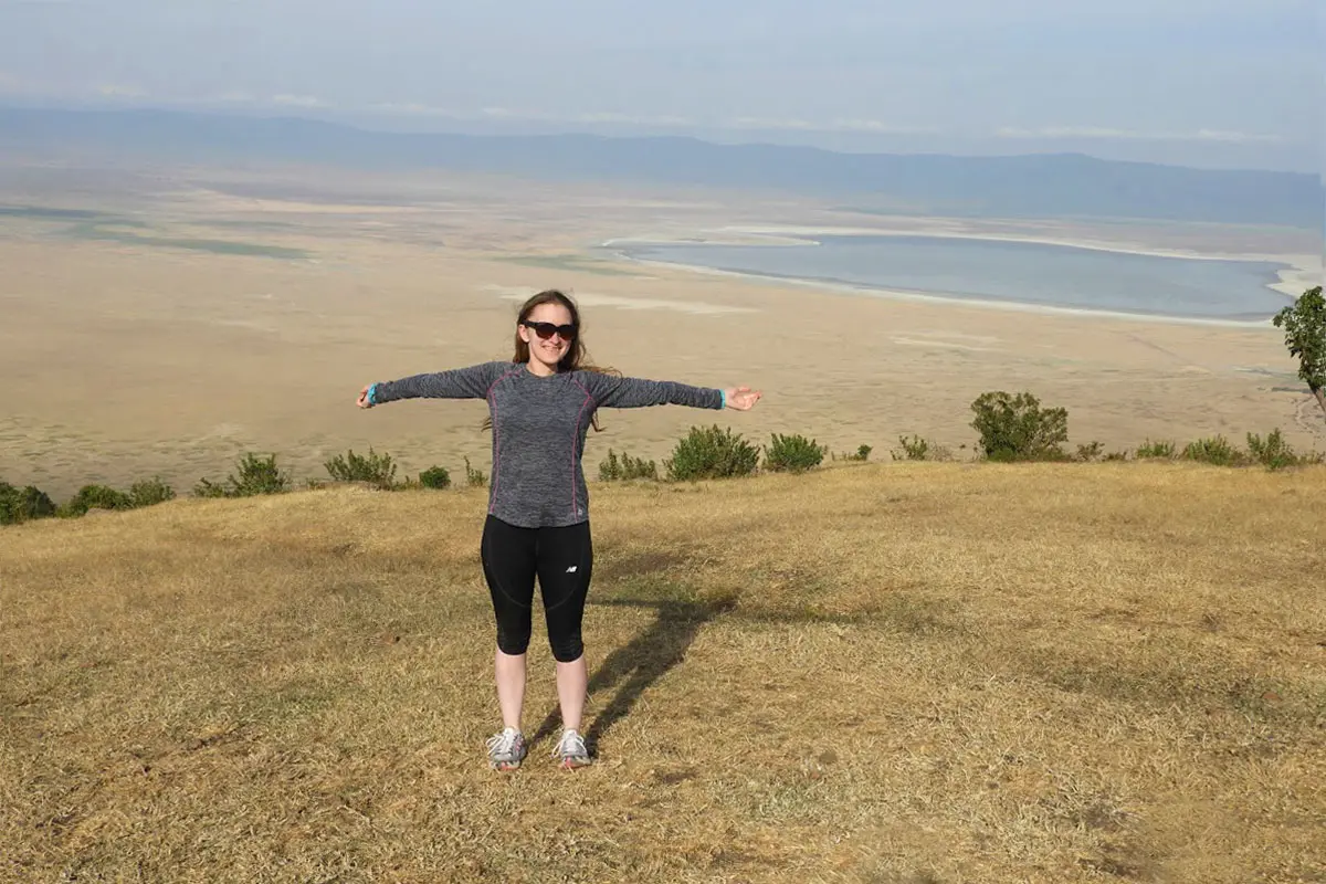 Guest with outstretched arms on the rim of Ngorongoro Crater, the crater floor and lake below