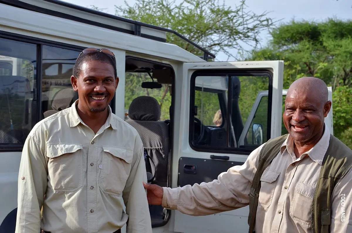 Two smiling Thomson guides standing beside a safari vehicle