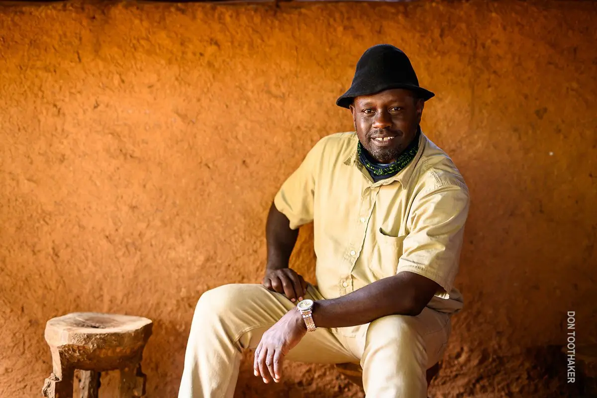 Thomson guide in a hat sitting on a stool against an orange wall