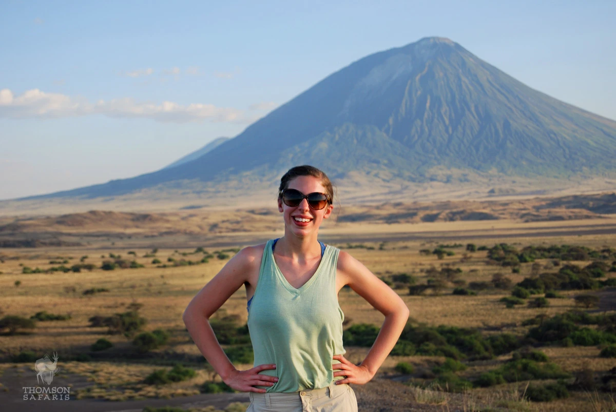 Guest standing on a ridge with the volcano Ol Doinyo Lengai rising behind her