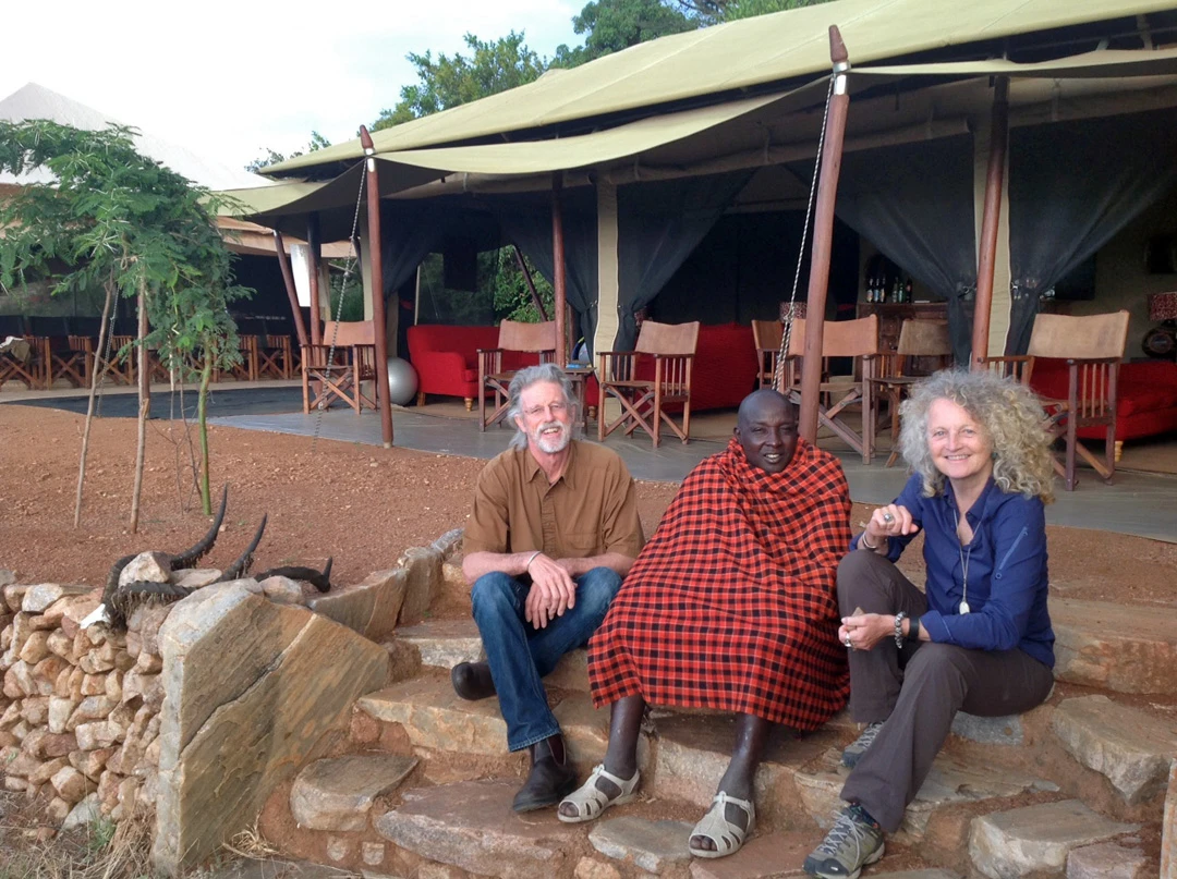 Rick Thomson and Judi Wineland sitting on stone steps at camp with a Maasai man