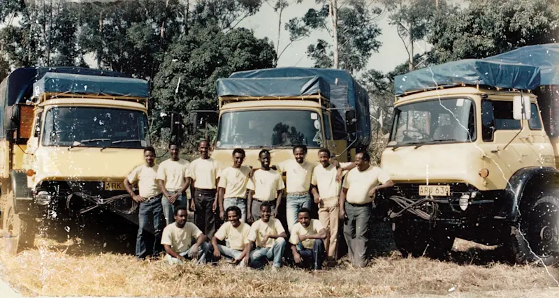 Faded vintage print of original Thomson staff lined up in front of three Bedford trucks