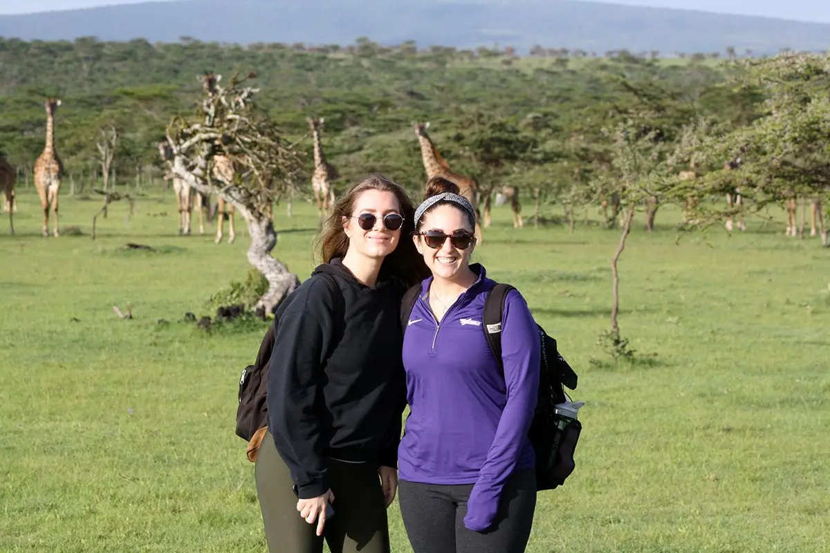 Two Thomson staff members posing on grassland with giraffes behind them