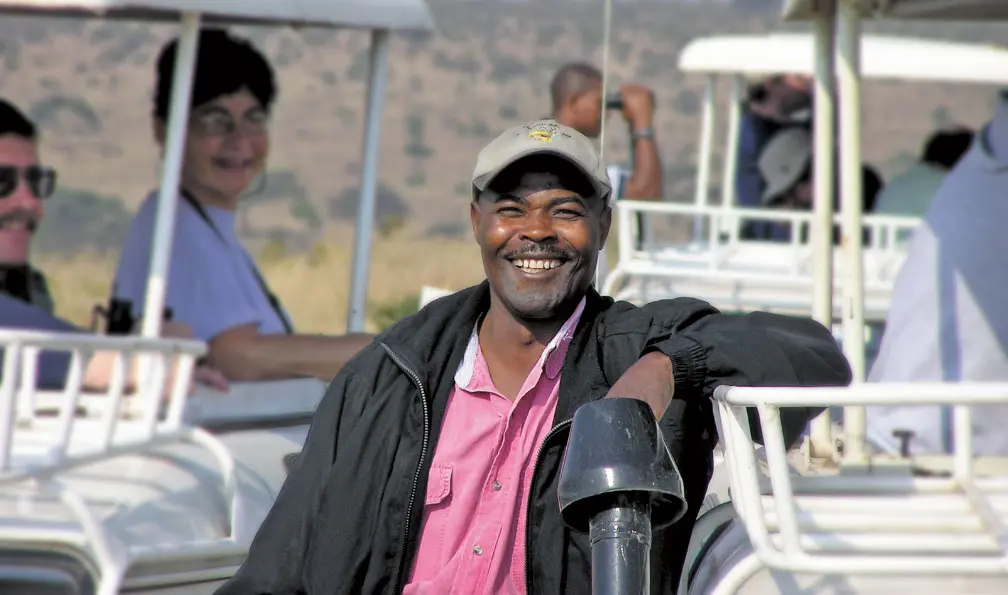Smiling Thomson guide leaning on an open-roof safari vehicle with guests