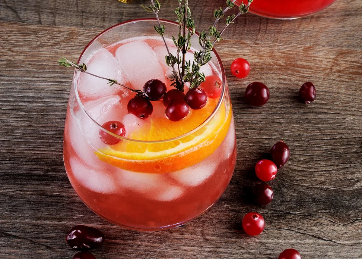 Cranberry orange gin and tonic with ice, orange slices and thyme on a wooden table