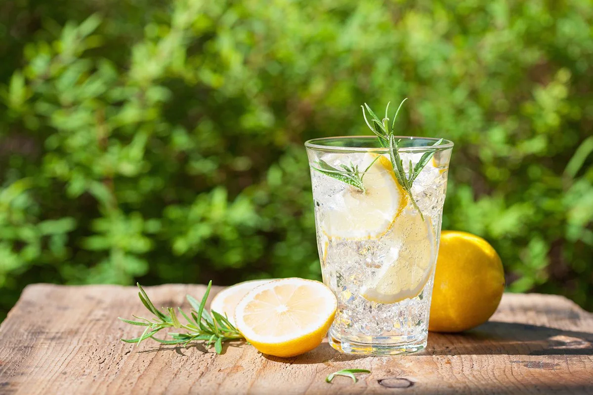 Sparkling lemon drink with ice and rosemary beside cut lemons on a wooden table