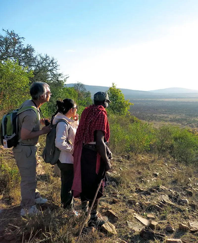 Maasai guide and two travelers looking out over a wide valley from a hillside