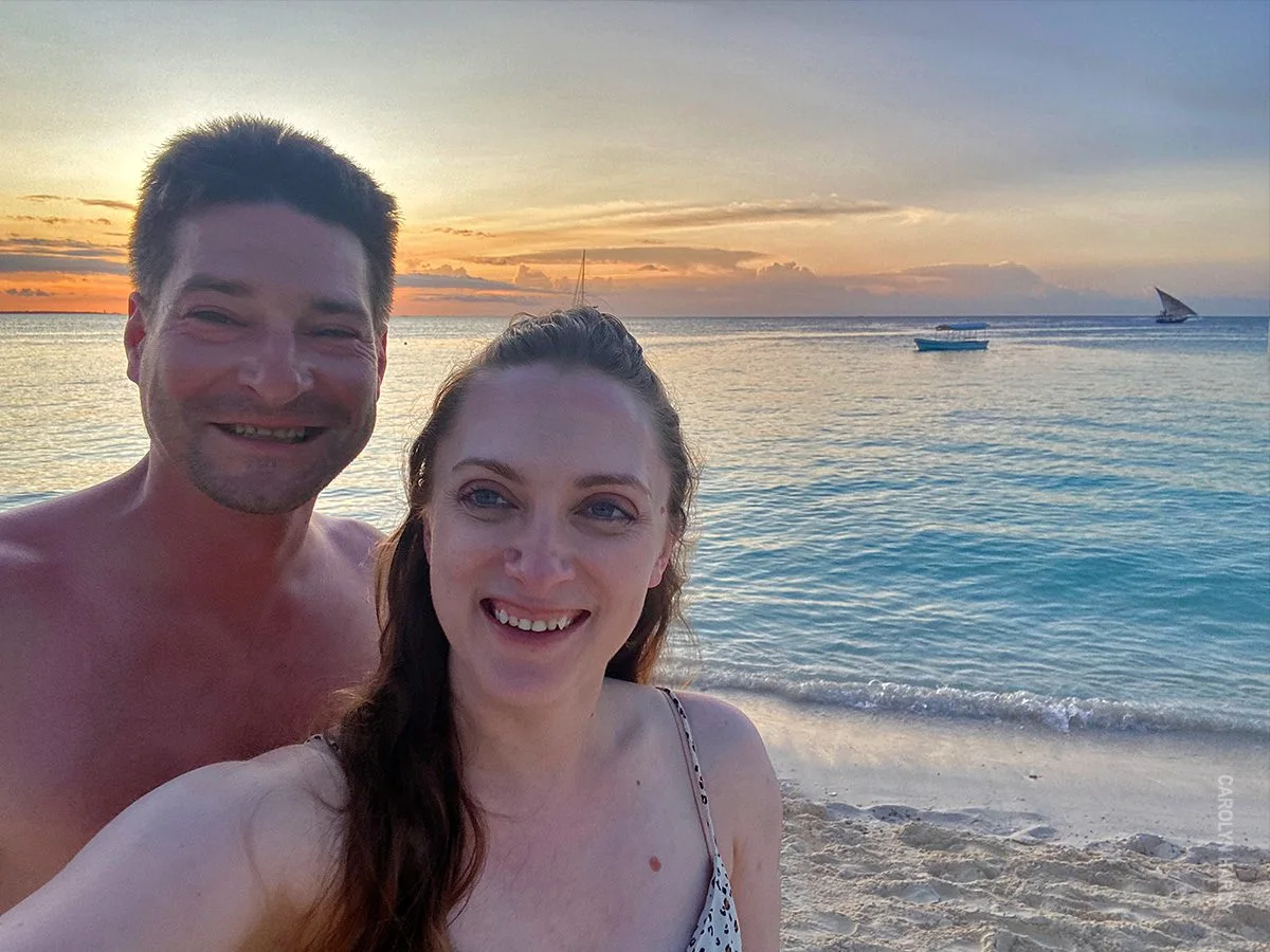 Couple taking a selfie on a Zanzibar beach at sunset with a dhow on the water