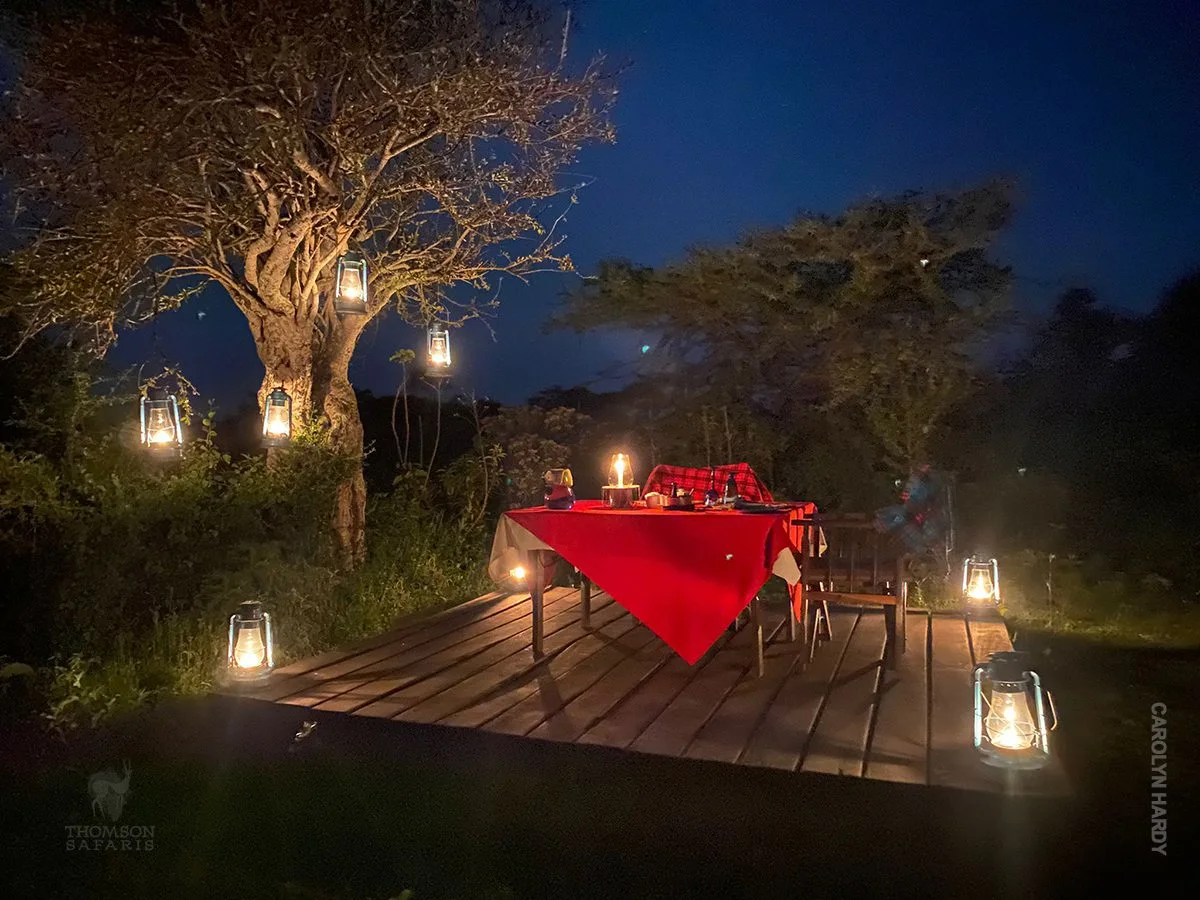 Candlelit dinner table on a wooden deck surrounded by lanterns at night