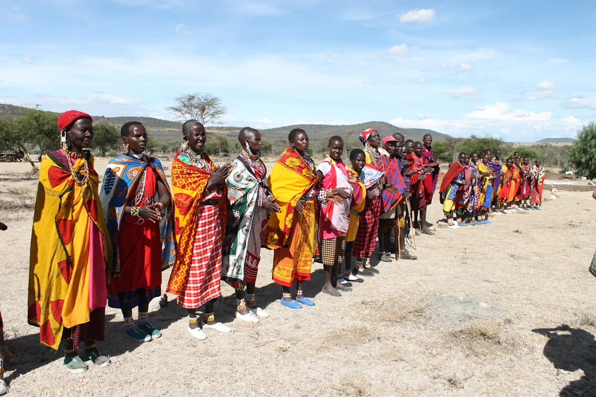 Maasai women in bright shukas and beaded jewelry standing in a long line