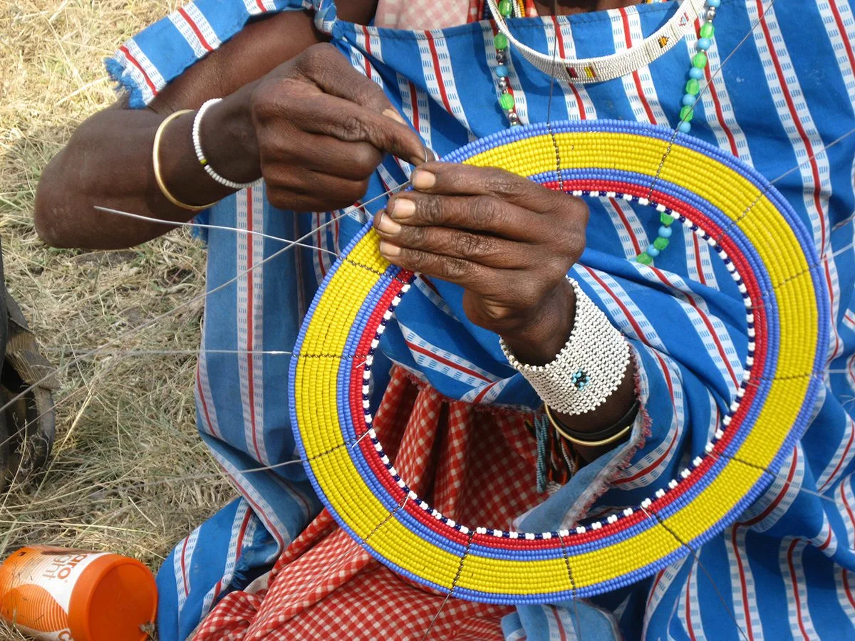 Hands of a Maasai woman stringing beads onto a yellow, red and blue beaded collar
