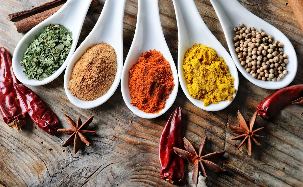 White spoons holding colorful ground spices with chilies and star anise on wood