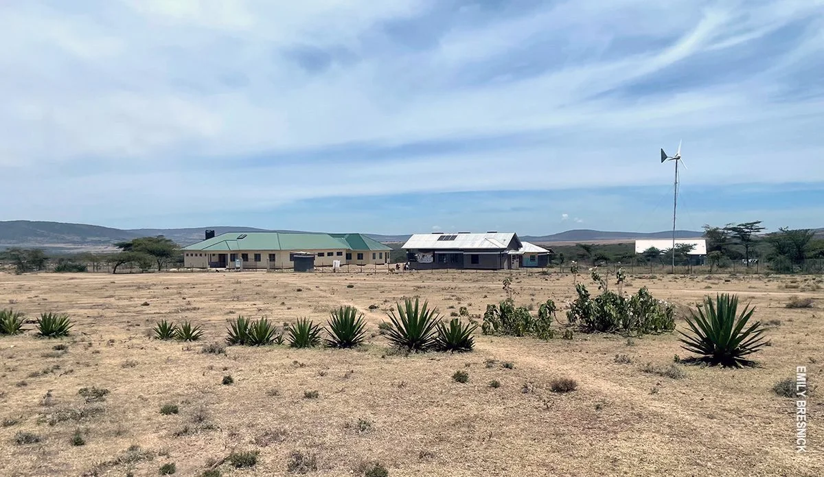 Clinic buildings and a wind turbine on dry plains with agave plants in front