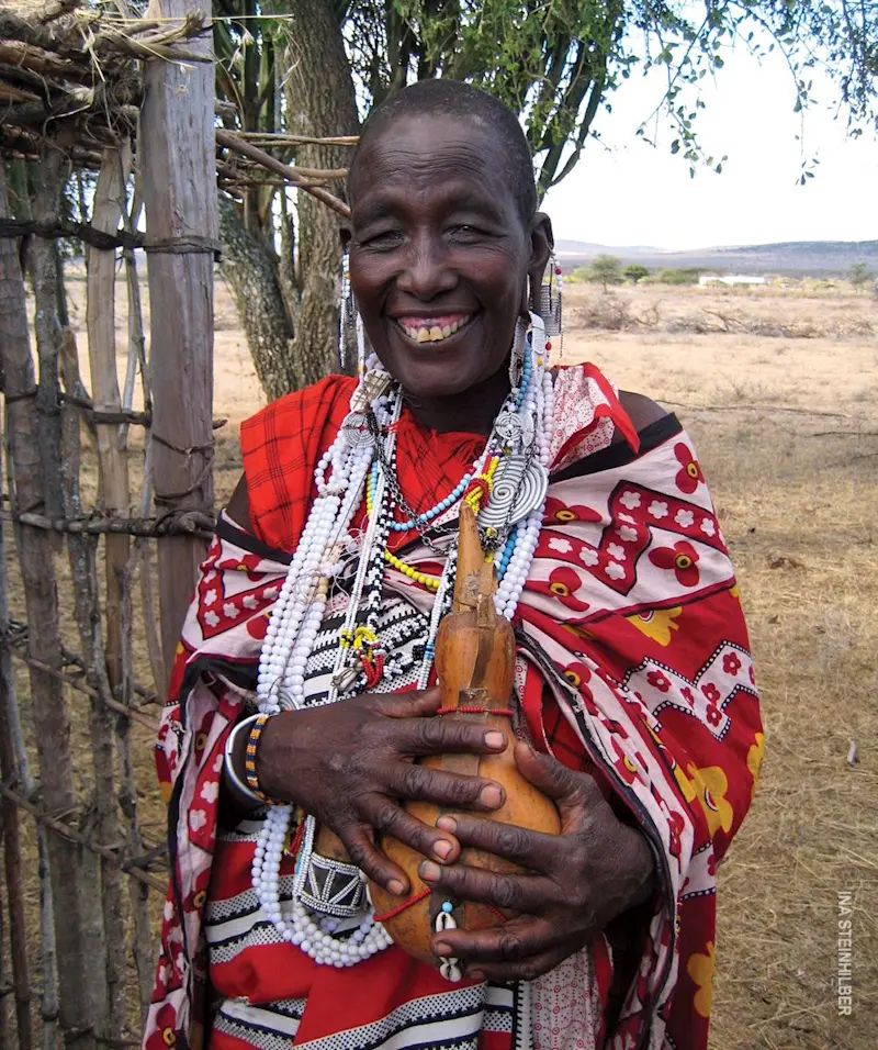 Smiling Maasai elder in a red shuka and beaded necklaces holding a carved gourd