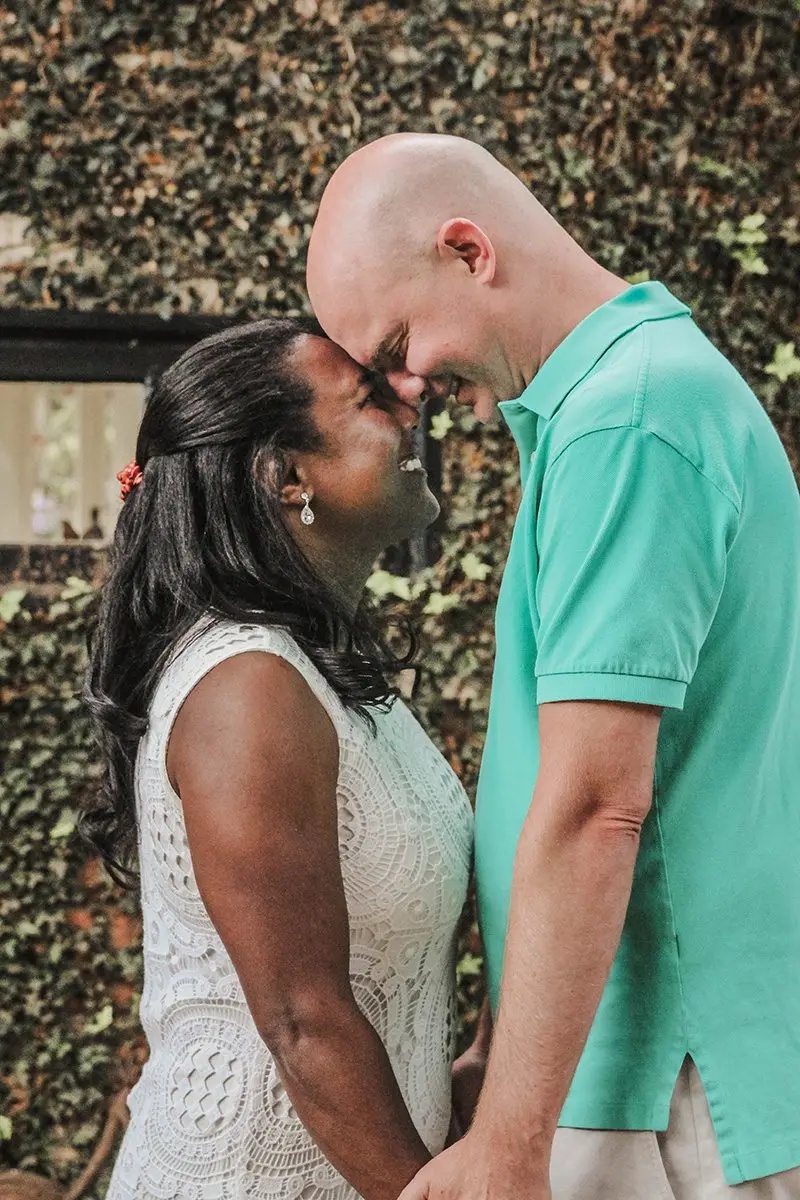 Smiling couple touching foreheads in front of an ivy-covered wall