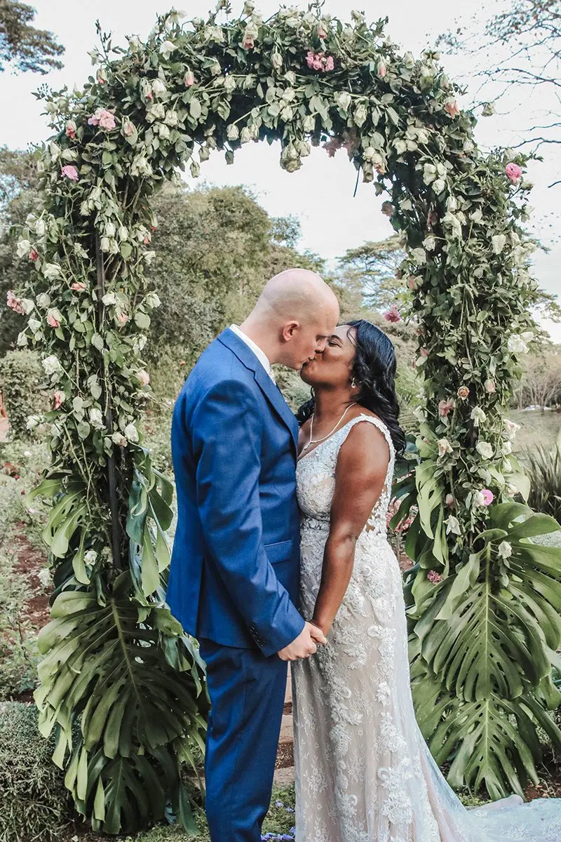 Bride and groom kissing under a floral arch at Gibb's Farm