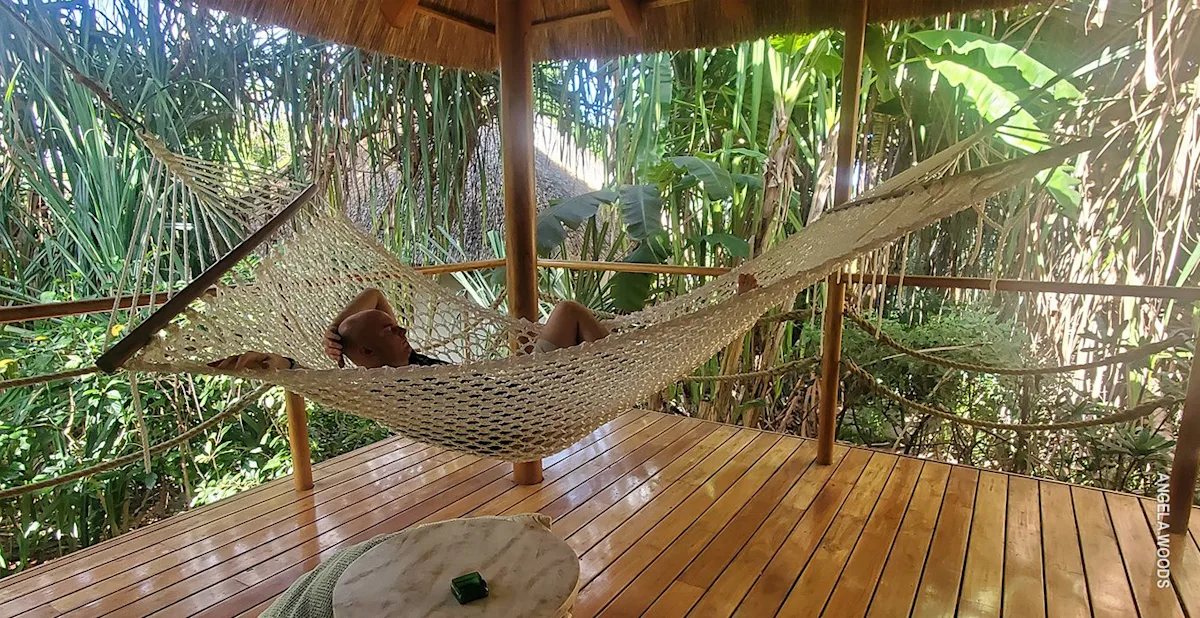 Man relaxing in a rope hammock on a wooden deck surrounded by tropical plants in Zanzibar