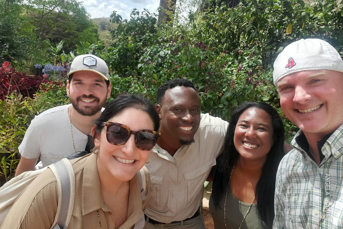 Smiling safari guide taking a group selfie with four travelers in a garden