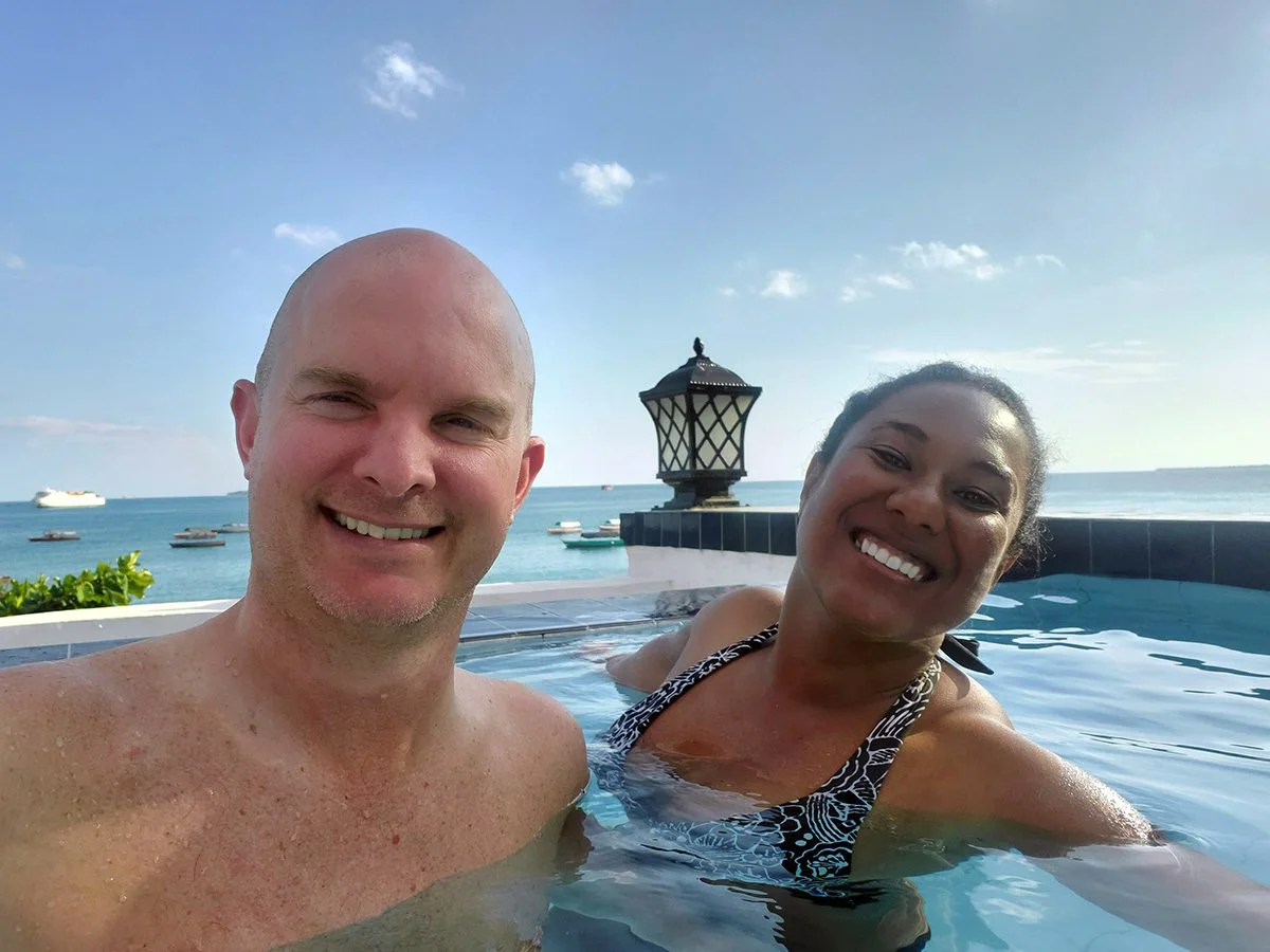 Smiling couple in an infinity pool overlooking the ocean and boats in Zanzibar