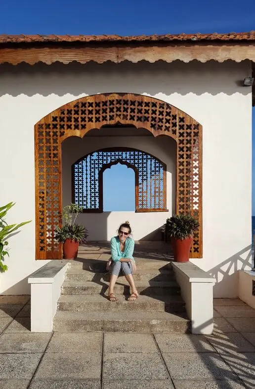 Guest sitting on the steps of a white archway with carved wooden screens in Zanzibar
