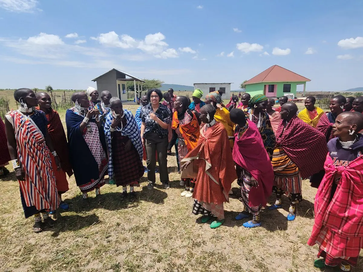Group of Maasai women in colorful shukas gathered with guests in a village
