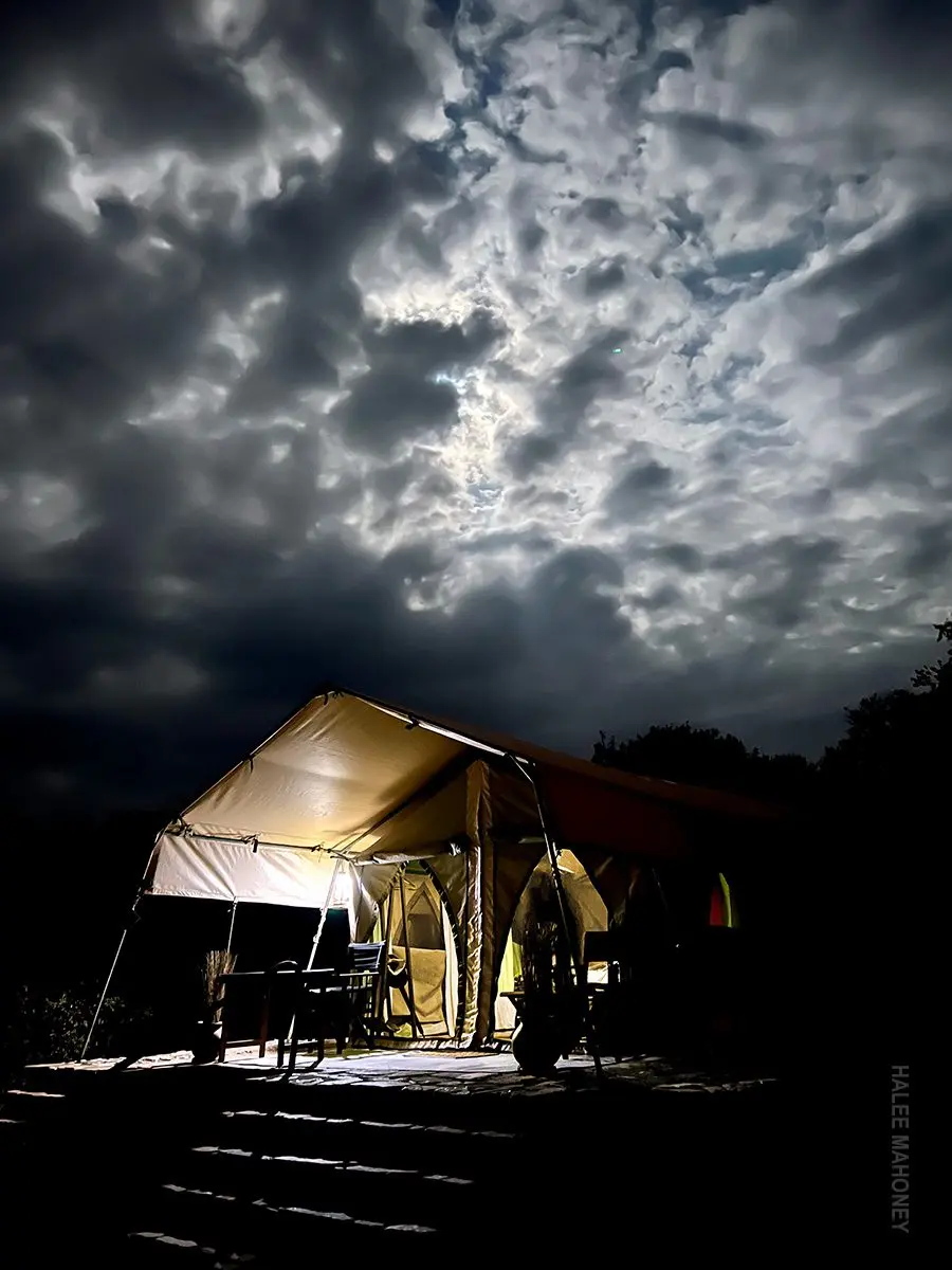Safari tent glowing with light at night under a dramatic cloudy sky