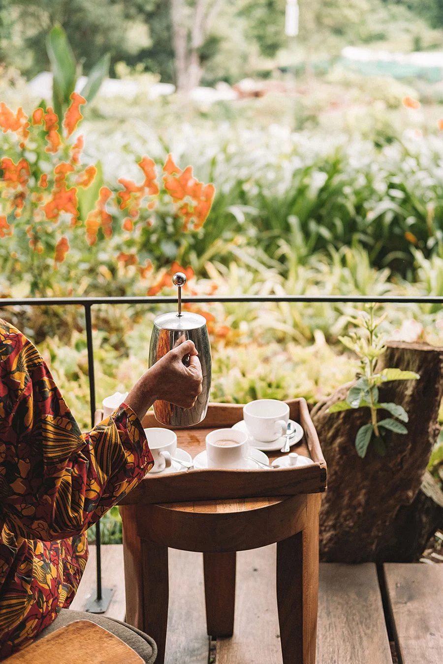 Coffee being poured from a French press on a verandah overlooking the Gibb's Farm gardens